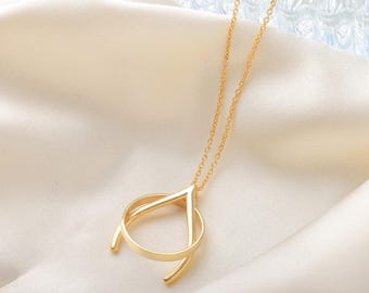 May include: A gold pendant necklace with an abstract design. The pendant combines geometric shapes, including a triangle and a circle, suspended from a delicate chain. The necklace is displayed on a soft, cream-coloured fabric. The chain and pendant are gold in colour.