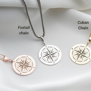 May include: Three circular compass pendants on chains. The left is a rose gold Figaro chain, the centre is a silver foxtail chain, and the right is a gold Cuban chain. Each pendant features a compass rose design with cardinal directions N, S, E, W.