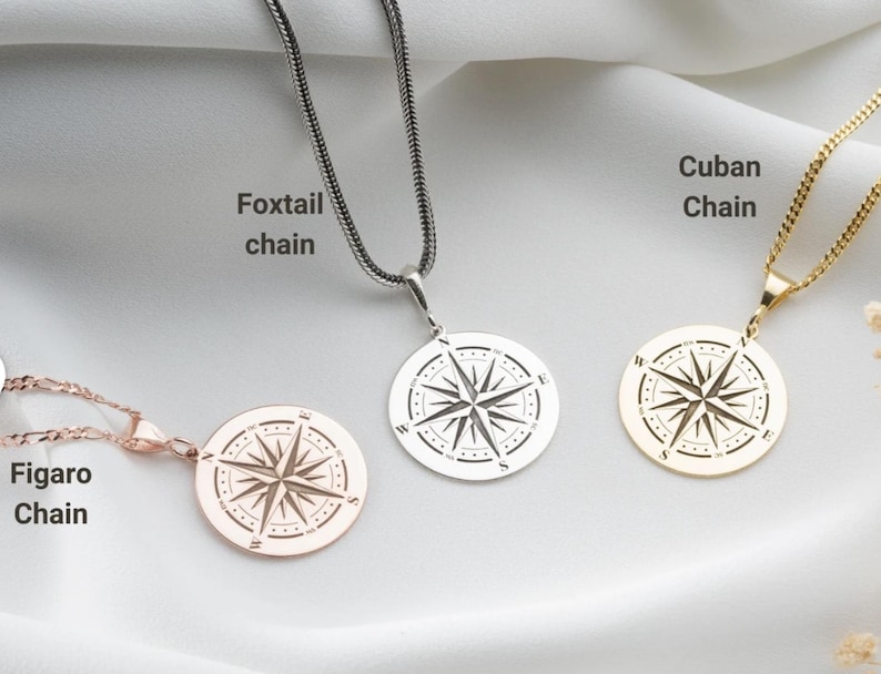 May include: Three circular compass pendants on chains. The left is a rose gold Figaro chain, the centre is a silver foxtail chain, and the right is a gold Cuban chain. Each pendant features a compass rose design with cardinal directions N, S, E, W.