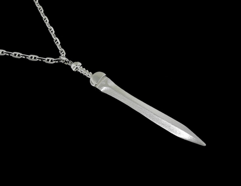 May include: A silver chain necklace with a silver sword pendant. The sword is detailed with a textured surface and a pointed tip.