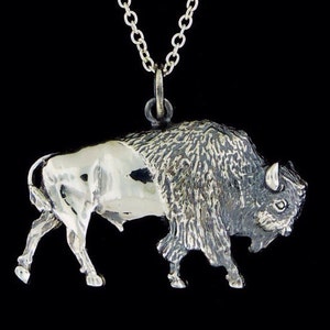 May include: A silver pendant necklace featuring a detailed, textured bison sculpture. The bison is depicted in a walking pose with its head turned to the side.