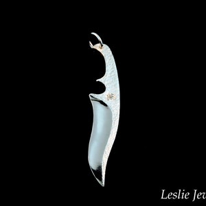 May include: A silver pendant shaped like a knife blade with a textured surface.