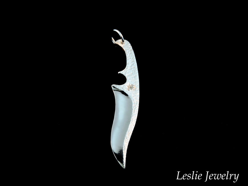 May include: A silver pendant shaped like a knife blade with a textured surface.