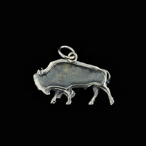 May include: Silver charm in the shape of a buffalo, with a loop for attaching to a necklace or bracelet.