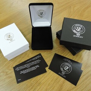 May include: Two black and white jewelry boxes with the logo "Leslie Jewelry" and a black card with the same logo and the text "Leslie Jewelry".