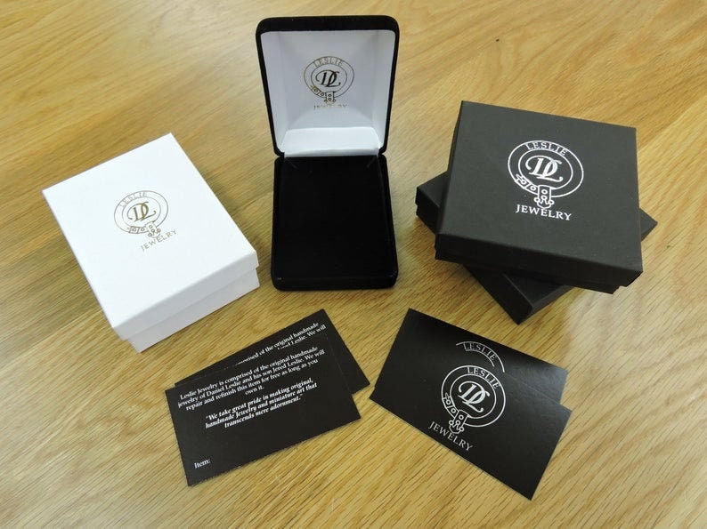 May include: Two black and white jewelry boxes with the logo "Leslie Jewelry" and a black card with the same logo and the text "Leslie Jewelry".