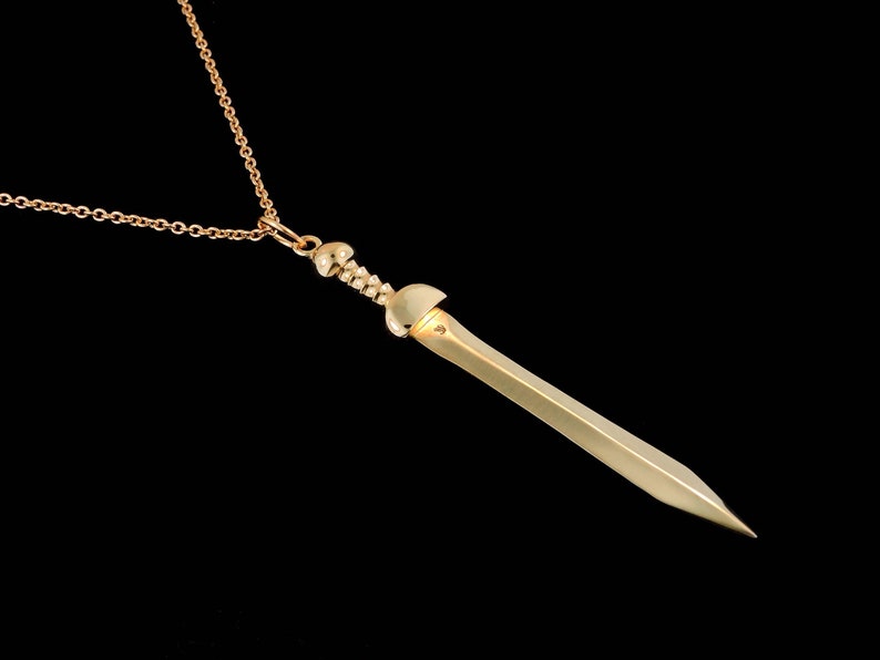 May include: A gold-toned necklace with a sword pendant. The sword has a detailed hilt and a sharp point.