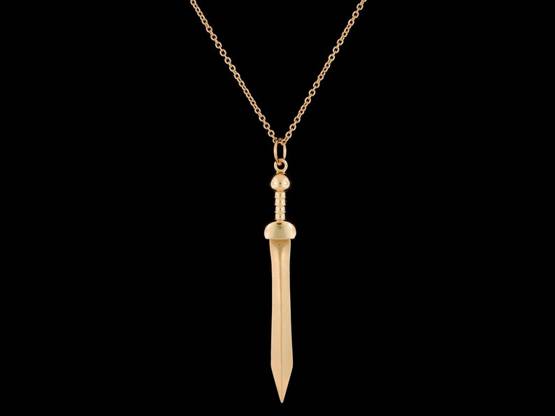 May include: A gold chain necklace with a gold sword pendant. The sword has a rounded tip and a detailed handle.