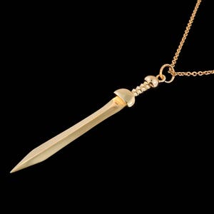 May include: A gold pendant necklace featuring a sword design. The sword is detailed with a pointed tip and a rounded hilt.