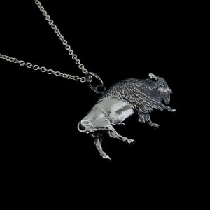 May include: A silver pendant necklace featuring a detailed bison sculpture. The bison is depicted in a running pose with its head turned to the side. The pendant is attached to a silver chain.