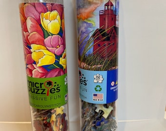 May include: Two clear plastic tubes with silver caps, each containing a micro puzzle. One tube features a floral design of pink, yellow, and red tulips. The other tube displays a red lighthouse scene. Each puzzle contains 150 pieces.