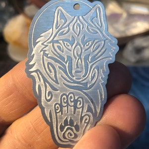 May include: A silver metal pendant featuring an intricate wolf design with a paw print below. The wolf's face is stylized with a tribal pattern.