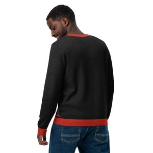 May include: A black long-sleeved sweater with a red trim around the neck and bottom hem. The sweater is made of a soft, comfortable material.