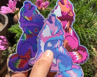 May include: Three die-cut stickers featuring stylized wolves howling at the sky. The stickers display vibrant color palettes including purple with rainbow glitter, blue and pink with a heart detail, and orange and pink with a holographic finish.