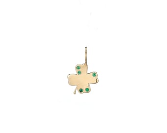 May include: A gold-colored clover pendant with four leaves and small green gemstones. The pendant has a loop at the top for hanging and is set against a white background. The clover design is a symbol of luck.