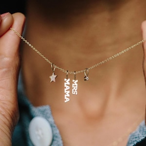May include: A delicate gold necklace with four charms. Charms include a star, the word "MAMA", the word "MRS", and a small round charm. The star charm is encrusted with small, sparkling stones.