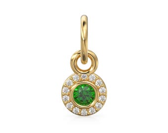 May include: A gold-colored pendant with a round, emerald-green gemstone center, surrounded by a halo of small, clear gemstones. The pendant has a loop at the top for attaching to a chain or bracelet.
