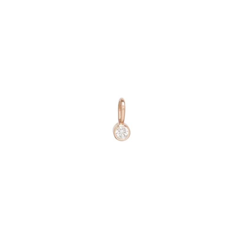 May include: A small, rose gold pendant with a single, round, clear gemstone. The pendant has a simple design with a loop at the top for attaching to a chain or bracelet. The gemstone is set in a bezel setting.