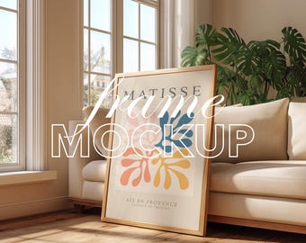 May include: A framed art print with a Matisse-inspired design in a light wood frame, leaning against a beige sofa. The artwork features the text "MATISSE" and "AIX EN PROVENCE". The room is bathed in sunlight. The words "Frame Mockup" are also visible.