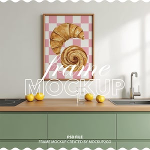 Könnte beinhalten: Ein gerahmter Kunstdruck mit einem Croissant und einem Gebäck auf einem rosa-weiß karierten Hintergrund. Der Rahmen ist braun. Der Text "frame MOCKUP" ist überlagert. Zitronen und ein Glas stehen auf der Küchentheke.