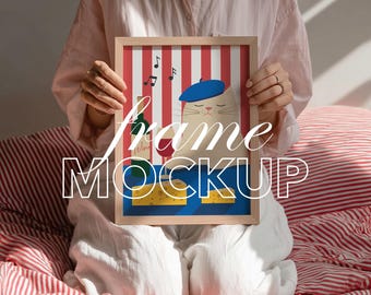 Op de afbeelding: Een ingelijste kunstdruk met een cartoonkat met een baret, wijn, kaas en muzieknoten op een rood-wit gestreepte achtergrond. De lijst is lichtbruin. De woorden "frame MOCKUP" worden weergegeven.