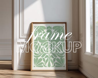 May include: A framed art print featuring a light green floral design on a white backdrop. The frame is light brown. The words "Frame Mockup" are overlaid. The print leans against a white wall, with a wooden floor.