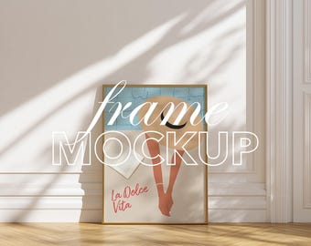 May include: A framed art print mockup featuring a gold frame. The artwork depicts a woman's arms and a straw hat, with the words "La Dolce Vita" in red. The image is set against a light blue background. The words "frame MOCKUP" are overlaid on the image.