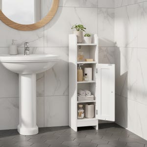 May include: A white, narrow bathroom cabinet with an open door, revealing shelves stocked with toiletries, towels, and decorative items. The cabinet is positioned next to a white pedestal sink and a round mirror. The bathroom has white marble-look tile.