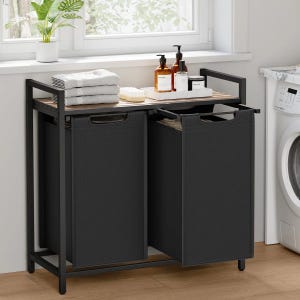 May include: A black laundry sorter with two compartments, a wooden top, and a black metal frame. The sorter has a pull-out design for easy access to the laundry bags. The top shelf holds towels, soap bottles, and a small plant.