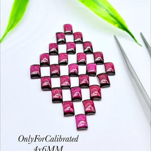 May include: A collection of deep magenta, rectangular-cut gemstones arranged in a diamond-shaped grid pattern. The stones are labelled as OnlyForCalibrated 4x6MM. A pair of silver metal tweezers is positioned to the right of the gemstone arrangement.