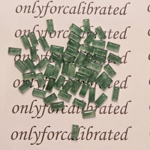 May include: A scattering of small, rectangular, translucent green beads on a white surface. The beads are slightly irregular in shape and have a polished look. The words "onlyforcalibrated" are printed in a cursive font.