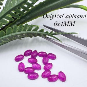 Könnte beinhalten: Eine Sammlung ovaler, leuchtend magentafarbener Edelsteine mit den Maßen 6x4mm. Die Steine werden zusammen mit einer Metallpinzette und einem grünen Farnblatt gezeigt. Der Text "OnlyForCalibrated 6x4MM" ist in der oberen rechten Ecke zu sehen.