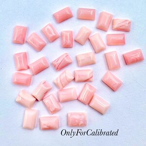 Peut inclure: Une collection de petits cabochons rectangulaires rose clair aux surfaces lisses et polies avec des motifs marbrés subtils. Les pierres sont disposées en formation dispersée, affichant diverses nuances de tons corail doux et rose poudré. OnlyForCalibrated.