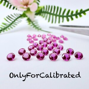 May include: A collection of small, round, faceted magenta gemstones arranged on a white surface. The text "OnlyForCalibrated" is printed in black at the bottom. A pair of metal tweezers and a small pink flower are visible in the background.