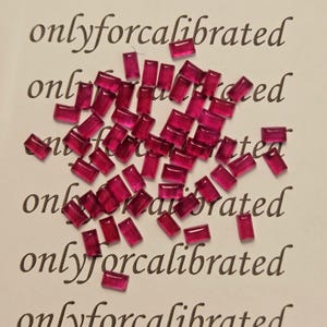 May include: A scattering of small, rectangular, ruby-red gemstones on a white background. The gemstones are translucent and polished. The words "onlyforcalibrated" are printed in a cursive font across the background.