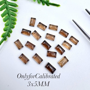 Könnte beinhalten: Eine Ansammlung kleiner, rechteckiger, durchscheinender brauner Edelsteine auf einer weißen Oberfläche. Die Steine sind facettiert und messen 3x5mm, wie durch den Text "OnlyforCalibrated 3x5MM" am unteren Bildrand angegeben.