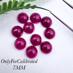 Könnte beinhalten: Neun runde, tief magentafarbene Cabochon-Edelsteine, die in einer Gruppe angeordnet sind. Jeder Stein hat eine glatte, polierte, gewölbte Oberfläche. Der Text "OnlyForCalibrated 7MM" ist unten links in Schwarz aufgedruckt und gibt die Größe an.