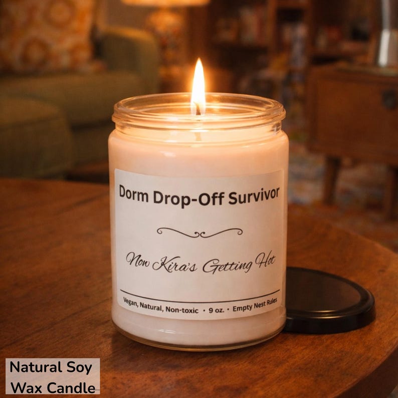 Puede incluir: Una vela de cera de soja encendida en un tarro de cristal con tapa negra. La etiqueta dice "Dorm Drop-Off Survivor" y "Now Kira's Getting Hot". La vela pesa 255 gramos y es vegana, natural y no t&oacute;xica.
