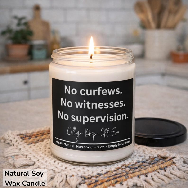 May include: A lit soy wax candle in a glass jar with a black label. The label reads "No curfews. No witnesses. No supervision." and "College Drop-Off Era." The candle is 9 oz and is vegan, natural, and non-toxic.