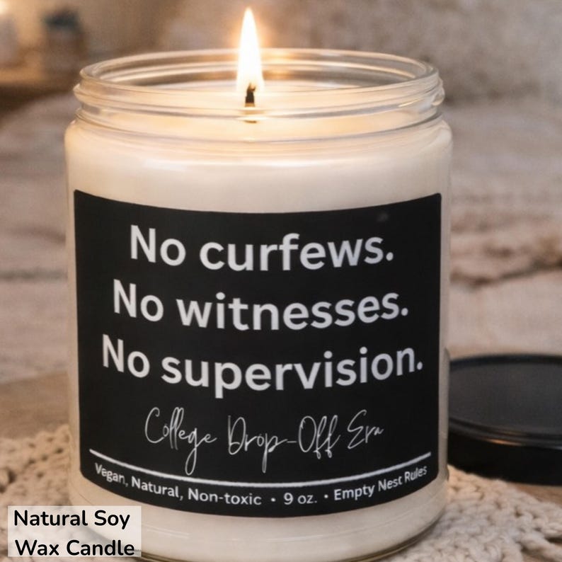May include: A lit soy wax candle in a glass jar with a black label. The label reads "No curfews. No witnesses. No supervision." and "College Drop-Off Era." The candle is 9 oz. and labeled as vegan, natural, and non-toxic.