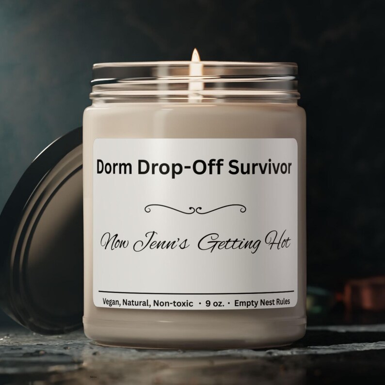 Puede incluir: Una vela encendida en un tarro de cristal con tapa plateada. La etiqueta dice "Dorm Drop-Off Survivor" y "Now Jenn's Getting Hot." La vela es de 255 gramos y est&aacute; etiquetada como vegana, natural y no t&oacute;xica.