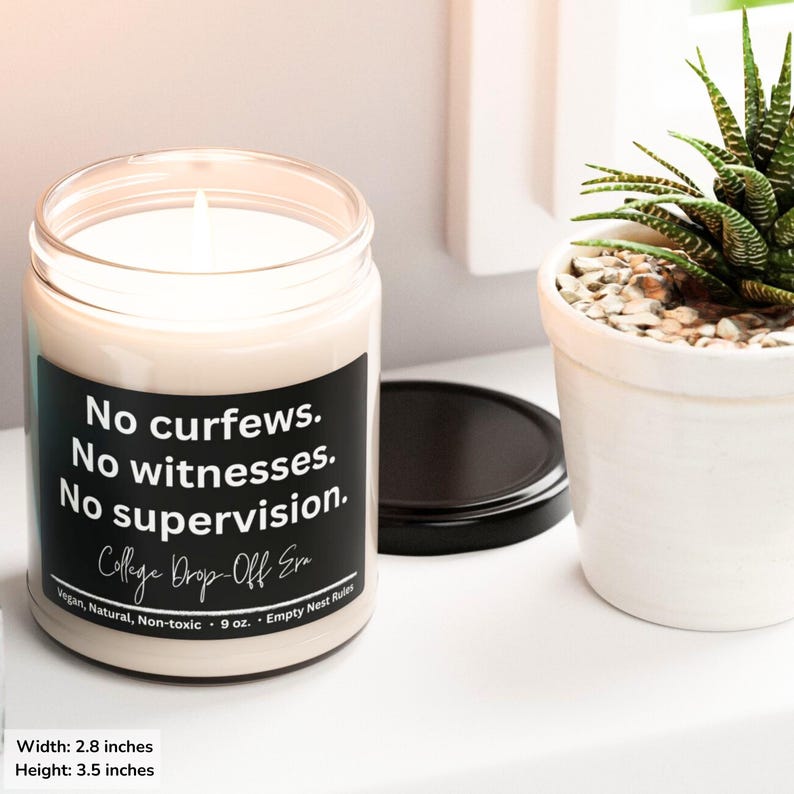 May include: A lit candle in a clear glass jar with a black label. The label reads "No curfews. No witnesses. No supervision. College Drop-Off Era." The candle is 2.8 inches wide and 3.5 inches high. A small potted plant is next to the candle.
