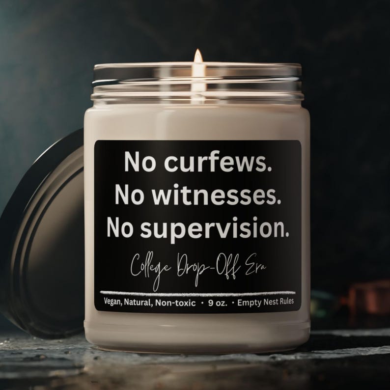 May include: A lit candle in a glass jar with a black label. The label reads "No curfews. No witnesses. No supervision. College Drop-Off Era." The candle is 9 oz and is vegan, natural, and non-toxic.