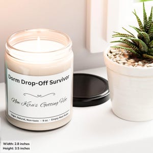 Puede incluir: Una vela en tarro de cristal transparente con una etiqueta blanca que dice "Dorm Drop-Off Survivor" y "Now Kira's Getting Hot". La vela mide aproximadamente 7,1 cm de ancho y 8,9 cm de alto. Una peque&ntilde;a planta suculenta en maceta est&aacute; al lado de la vela.