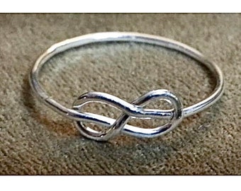 Könnte beinhalten: Ein silberner Ring mit einem Unendlichkeitsknoten. Der Ring ist schlicht und elegant mit einer glatten Oberfläche.