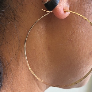 May include: Gold hoop earrings with a hammered finish. The earrings are large and have a simple, elegant design.