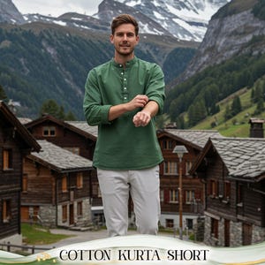 May include: A green cotton kurta short with a mandarin collar and button-down front. The model is wearing the shirt with light gray pants. The text "COTTON KURTA SHORT" is at the bottom of the image. The background features a mountain range and wooden buildings.