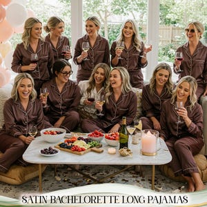 May include: A group of women in matching brown satin pajamas, holding wine glasses, and smiling. The pajamas have white piping. A table in front holds snacks and drinks. The text "SATIN BACHELORETTE LONG PAJAMAS" is at the bottom.
