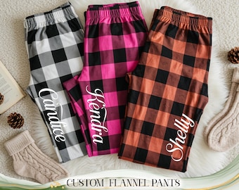 May include: Three pairs of custom flannel pants in black and white, hot pink and black, and orange and black buffalo plaid patterns. Each pair has a name printed on the leg. The text "CUSTOM FLANNEL PANTS" is at the bottom.