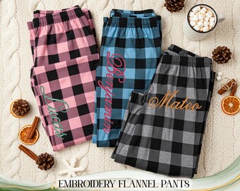 May include: Three pairs of embroidered flannel pajama pants in pink, blue, and gray, each with a name embroidered on them. The pants have a classic black and white buffalo check pattern. The words "Embroidery Flannel Pants" are at the bottom of the image.